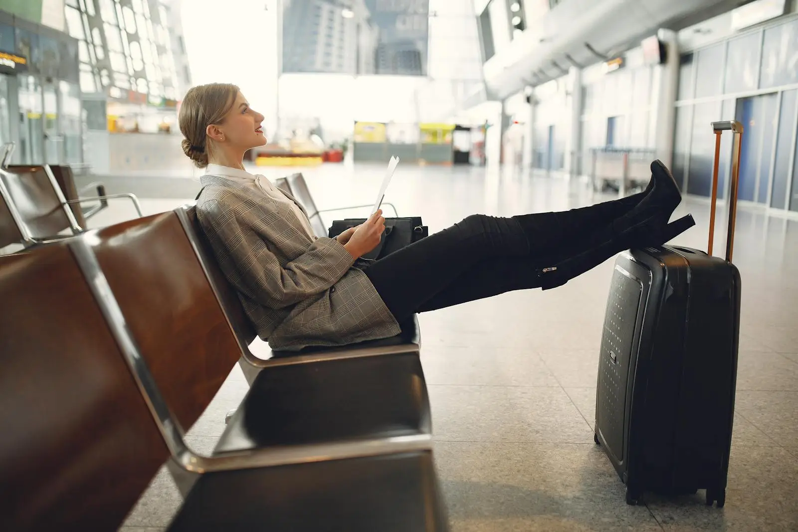 A woman relaxes in an airport terminal waiting area, reading a tablet with luggage nearby.
