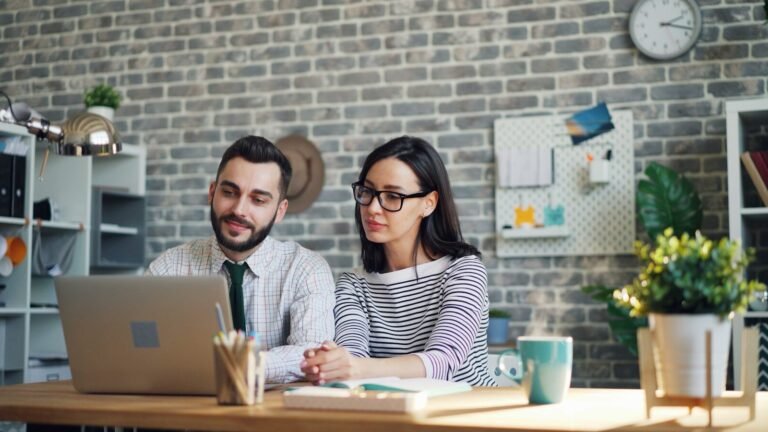 a man and woman sitting at a table looking at a laptop